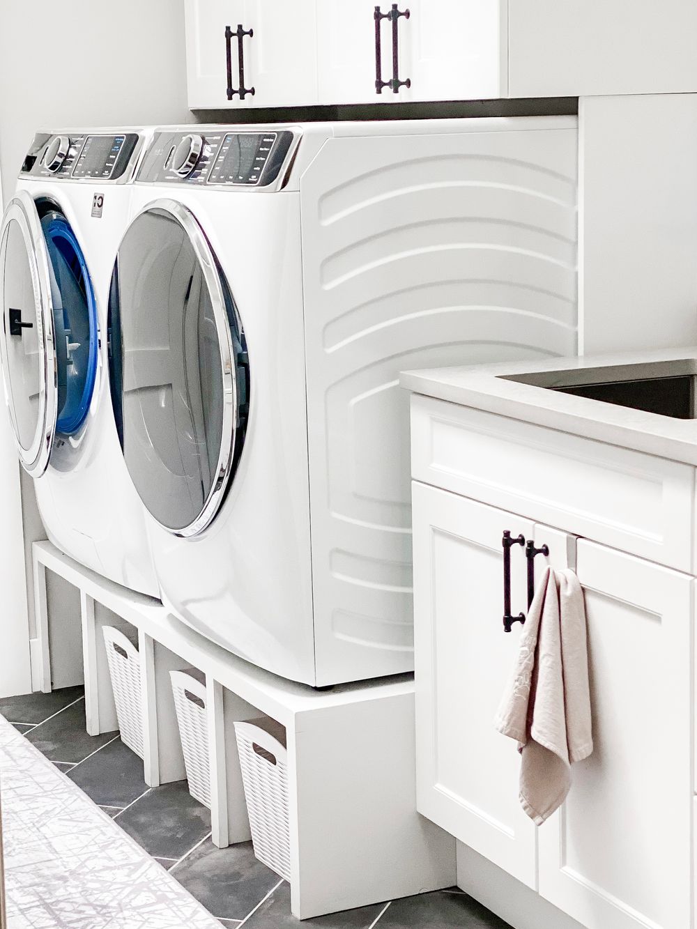 Clean white modern laundry room with multiple front-loading washers and built-in storage cabinets.