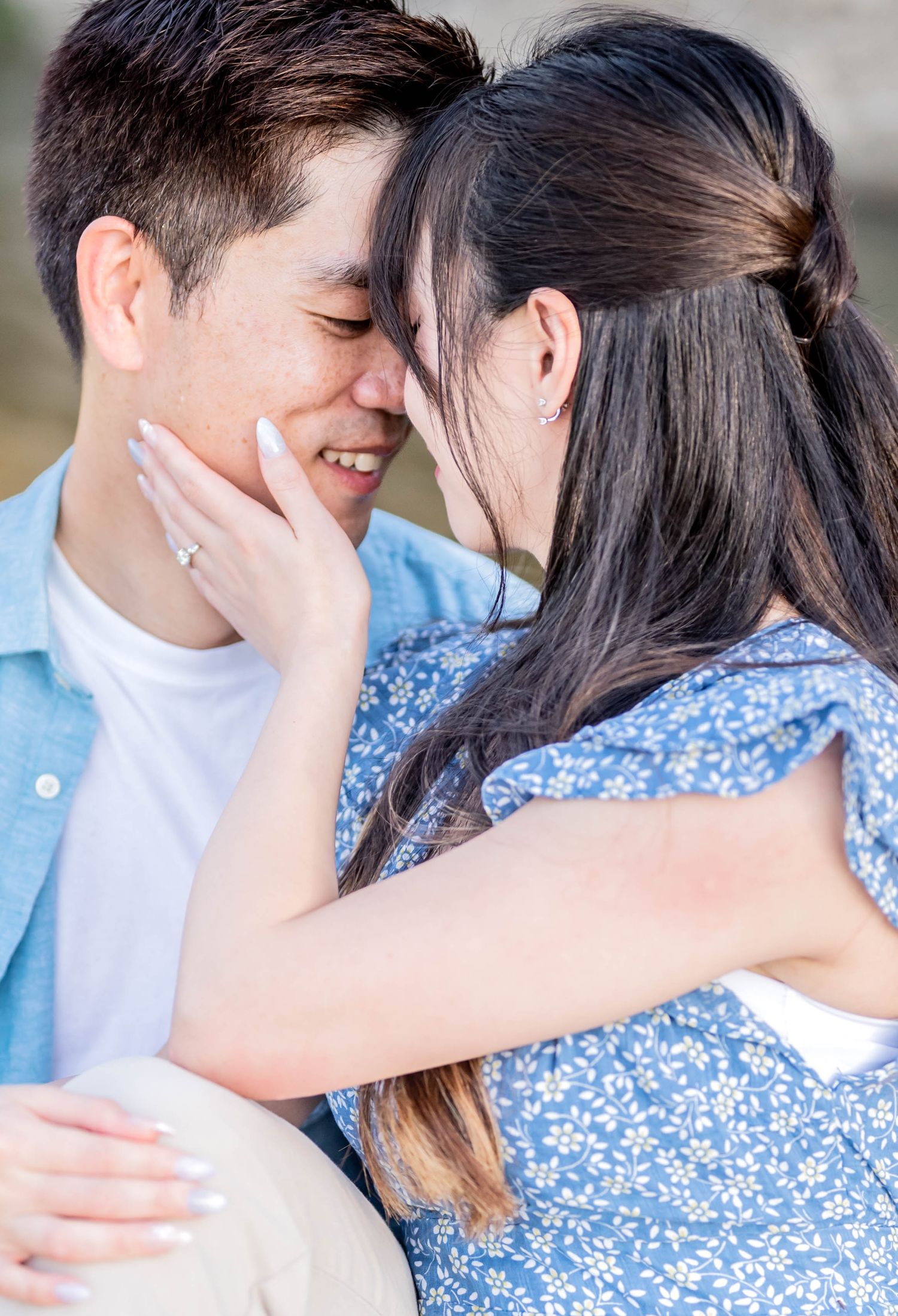 Romantic couple in blue floral dress and white shirt embrace during golden hour photoshoot outdoors.