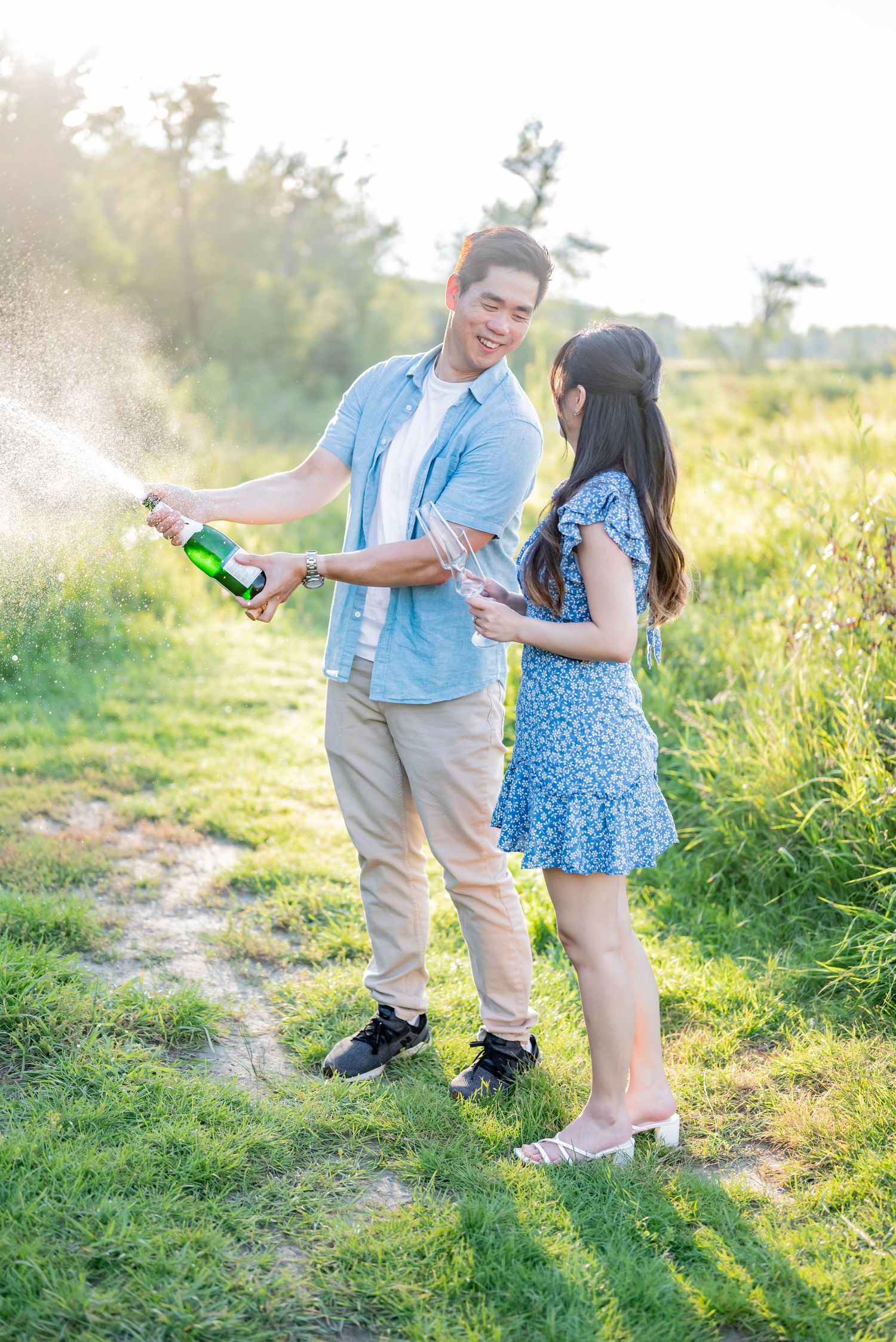 A couple walking together on a sunlit path surrounded by lush green vegetation and wildflowers.