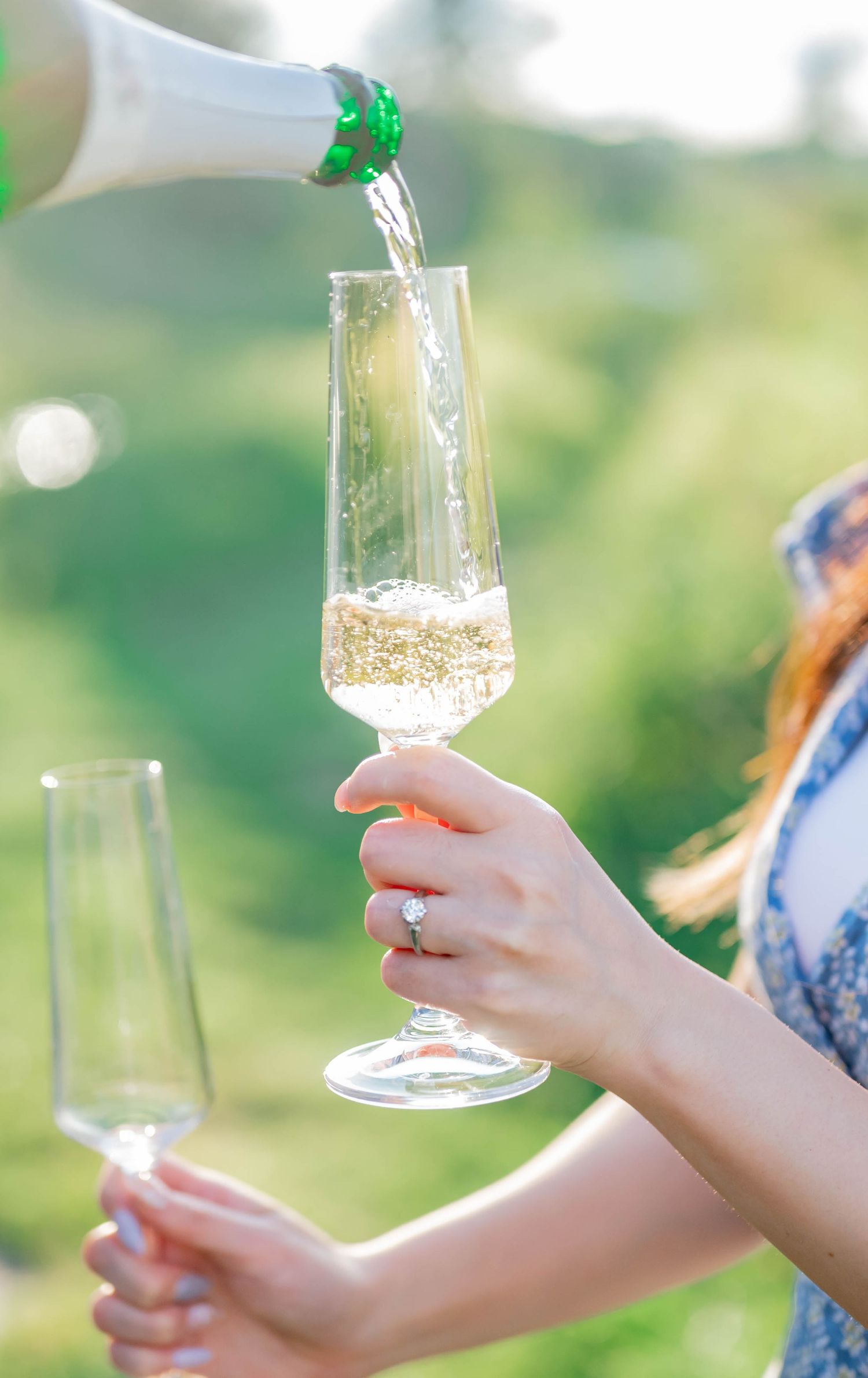 Champagne glasses being held up in sunlit outdoor celebration setting.