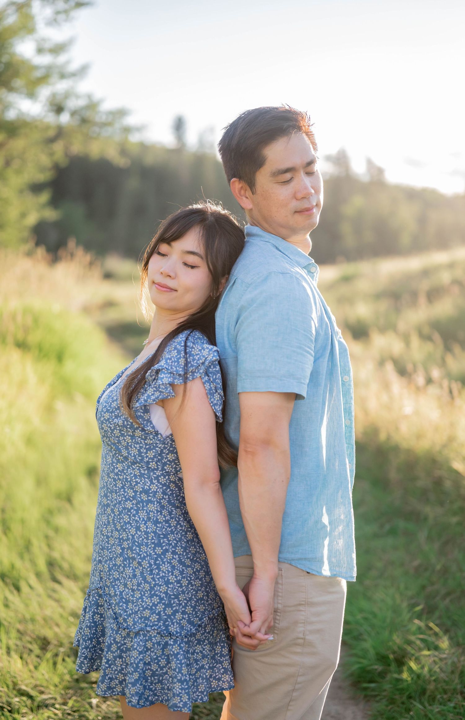 Romantic couple in blue and khaki outfits embracing in a sun-drenched meadow.