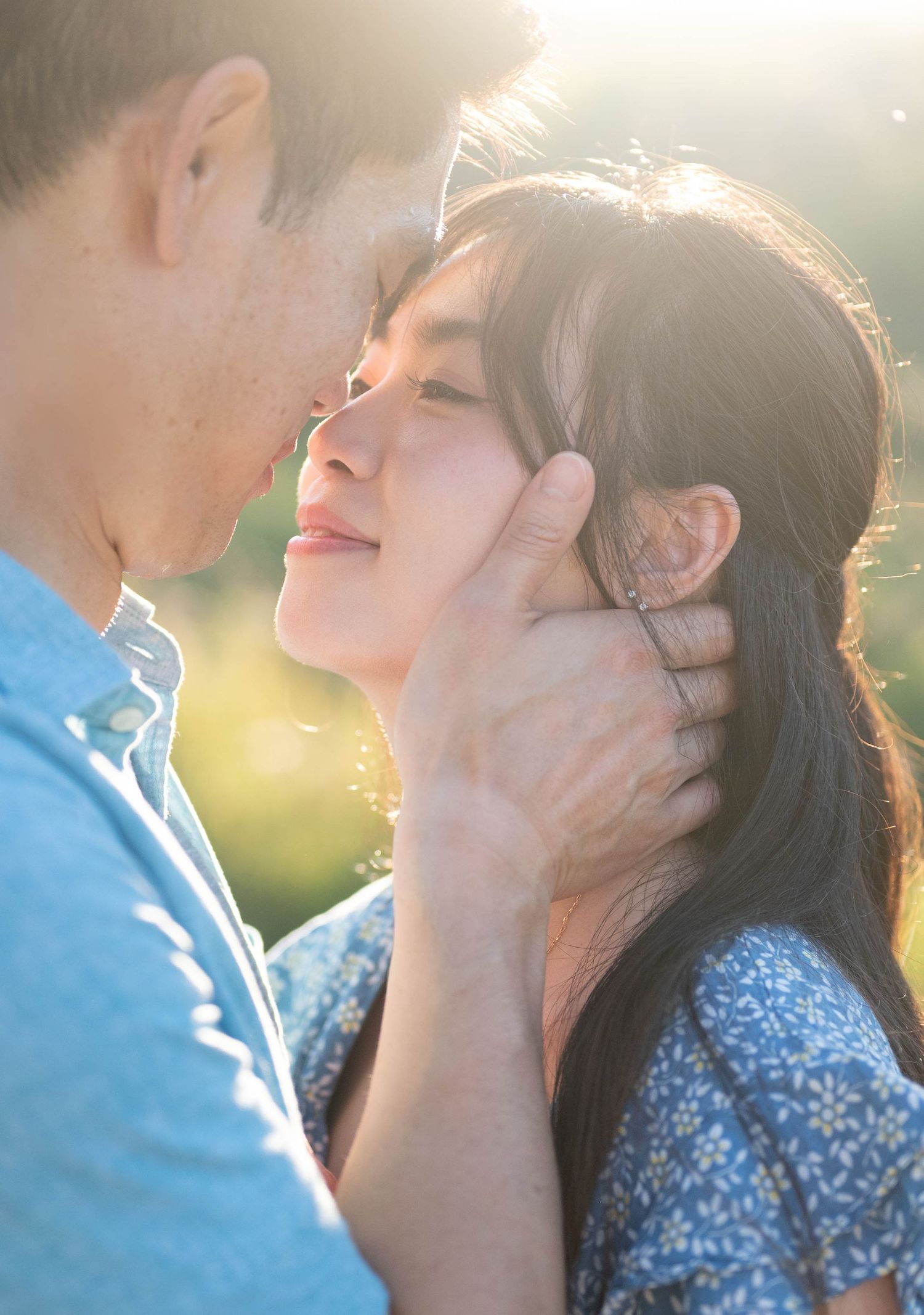 Two people sharing a tender romantic moment together in soft sunlit outdoor setting while wearing blue.