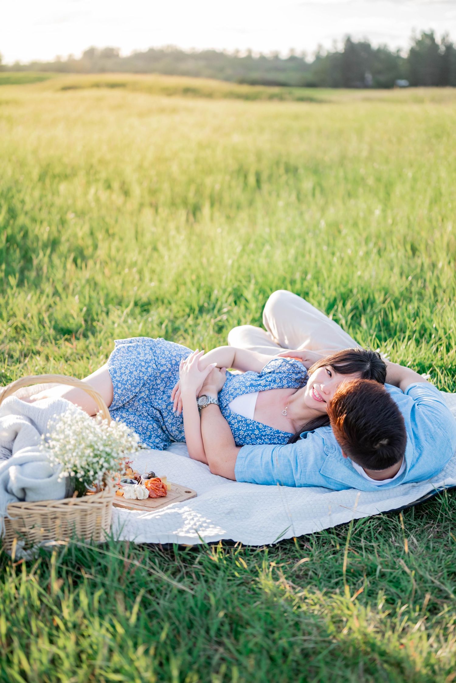 A romantic picnic scene with a white blanket and basket laid out in a sunlit meadow of tall grass.