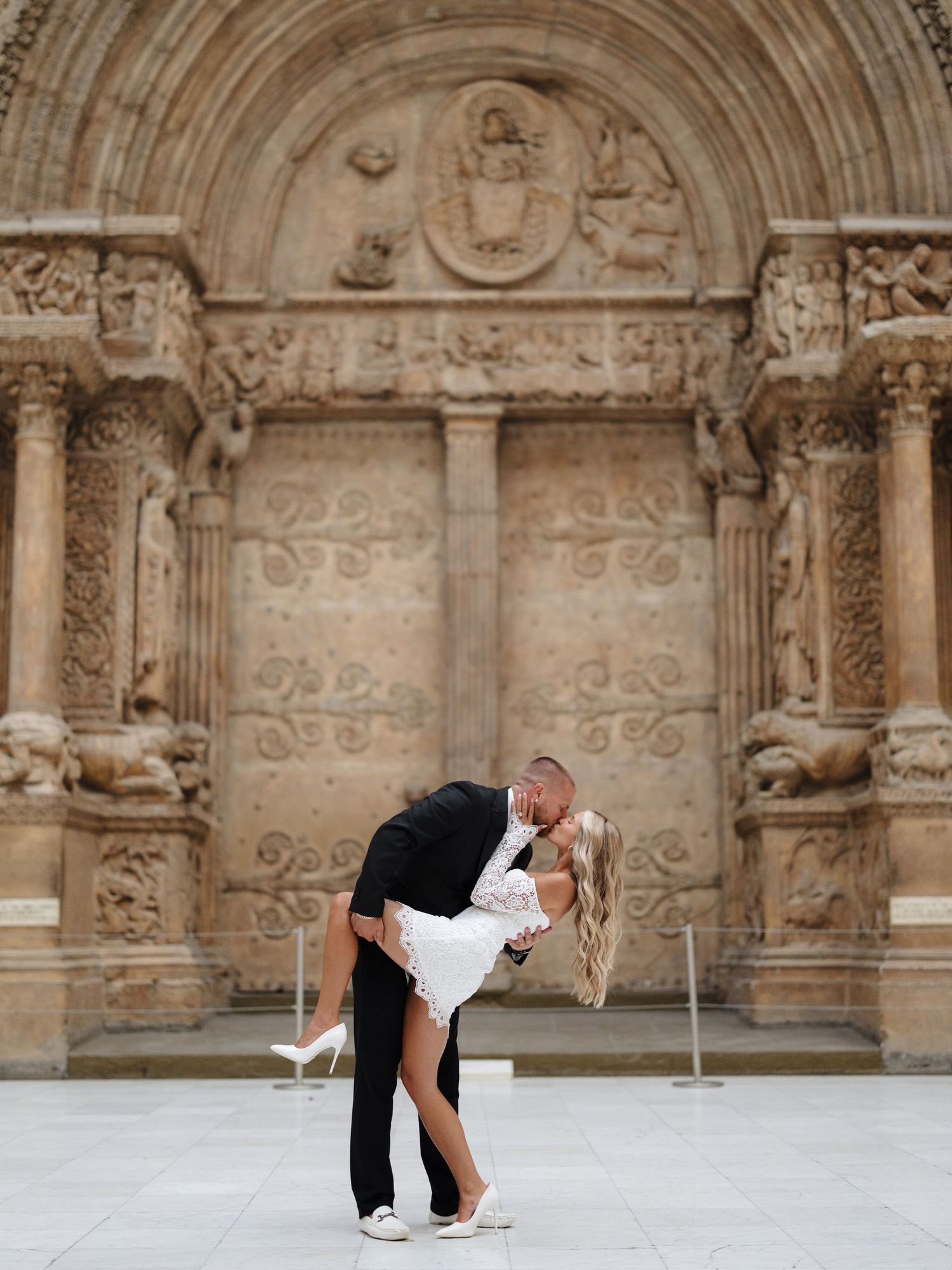 Couple shares romantic dip pose in front of ornate stone archway architecture during celebration photoshoot.