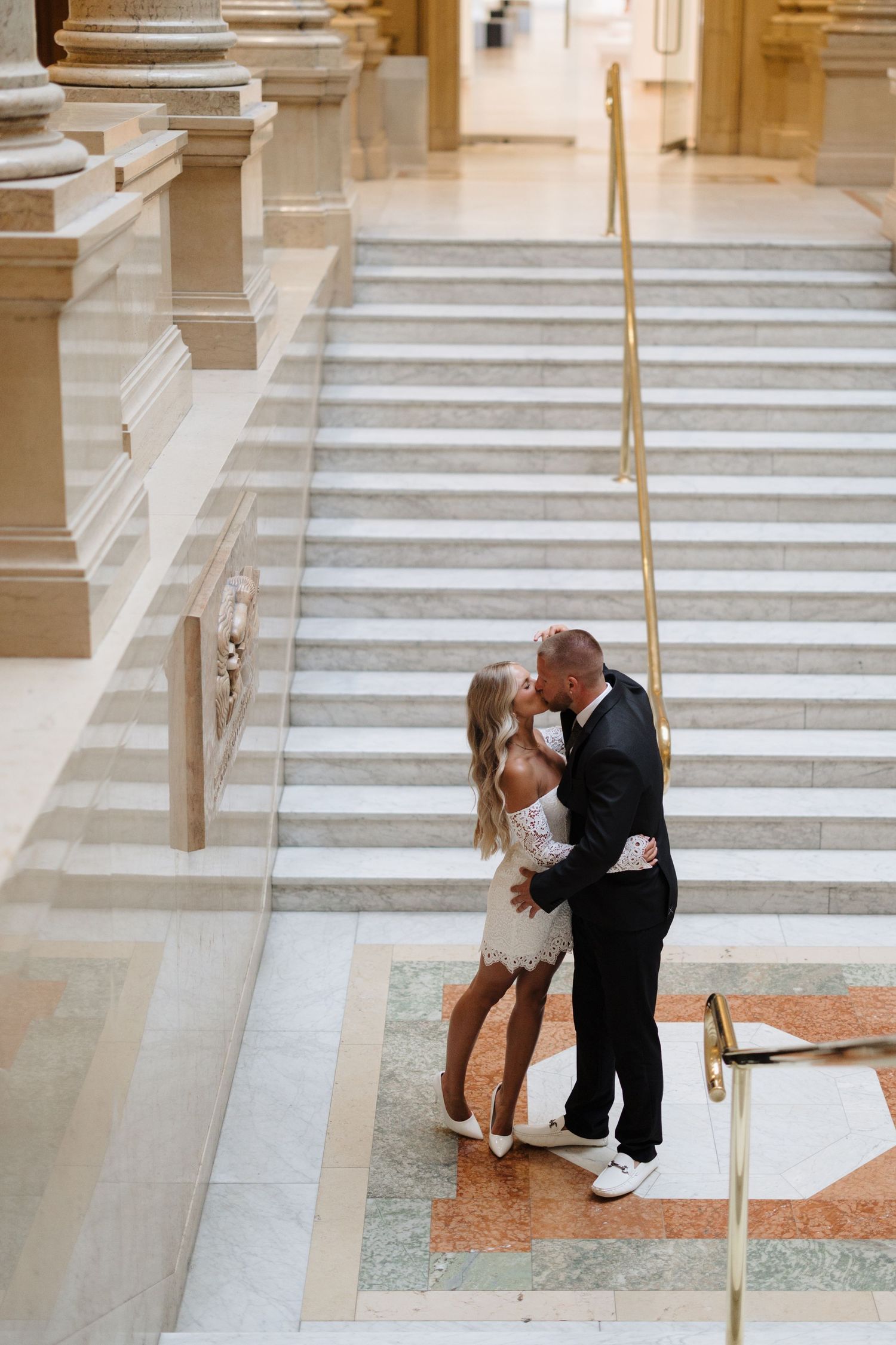 A couple shares a romantic moment on marble steps inside an elegant classical building.