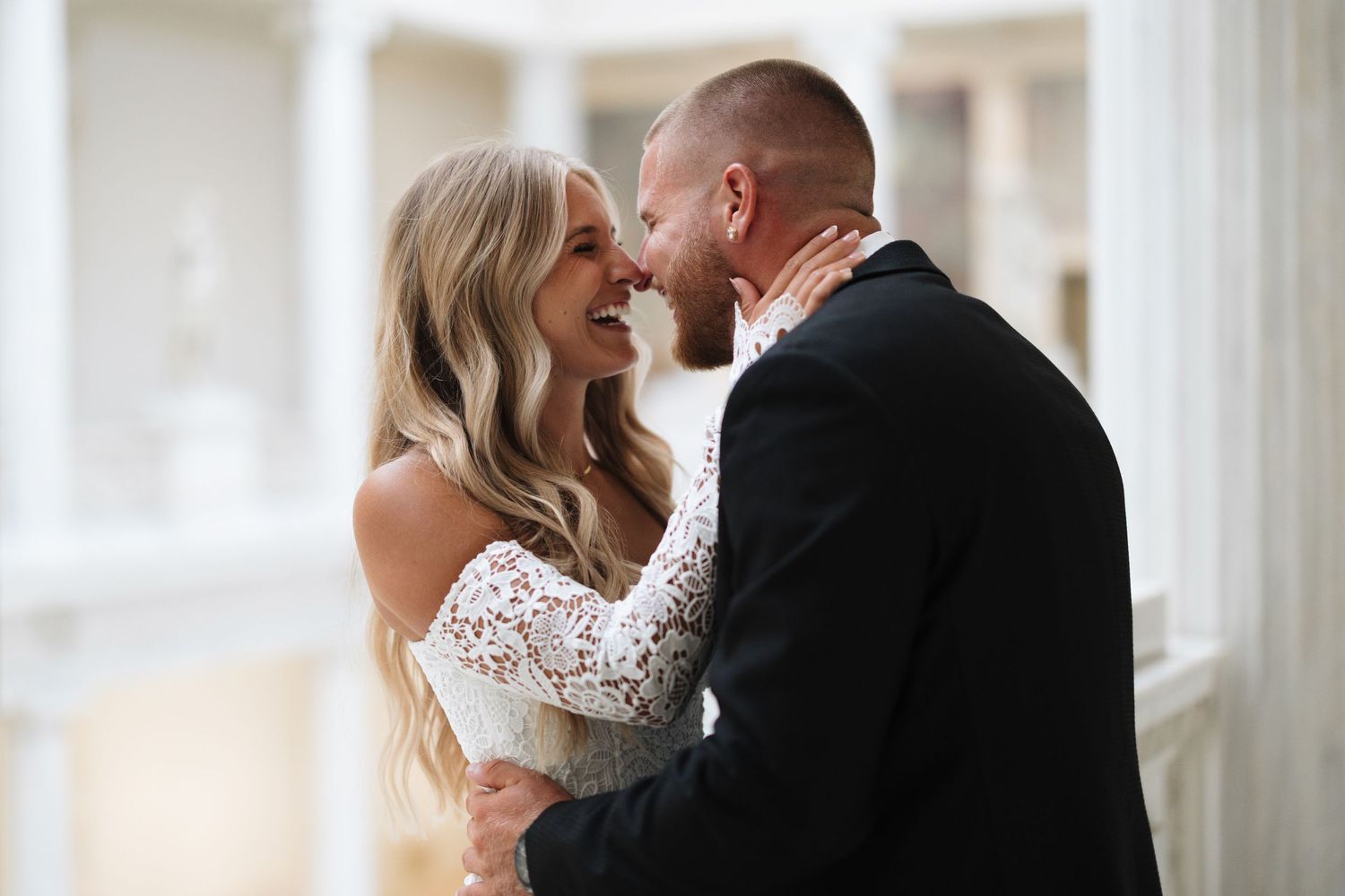 A couple in wedding attire shares a romantic moment with foreheads touching while softly smiling together.