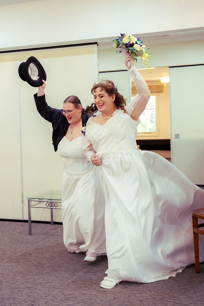 A joyful wedding celebration as two brides in white dresses dance and celebrate together on their special day.