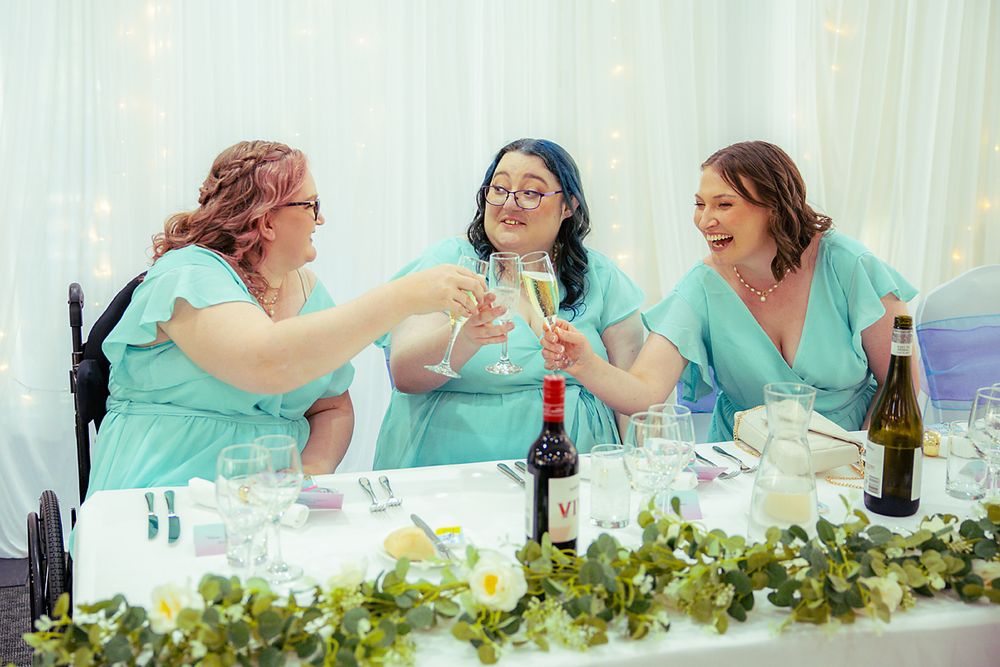 Wedding guests share laughter and conversation while seated at an elegant reception table with greenery decor.