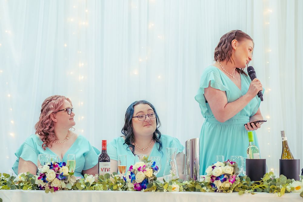 Two people in teal dresses smile and laugh while standing together at an outdoor celebration.