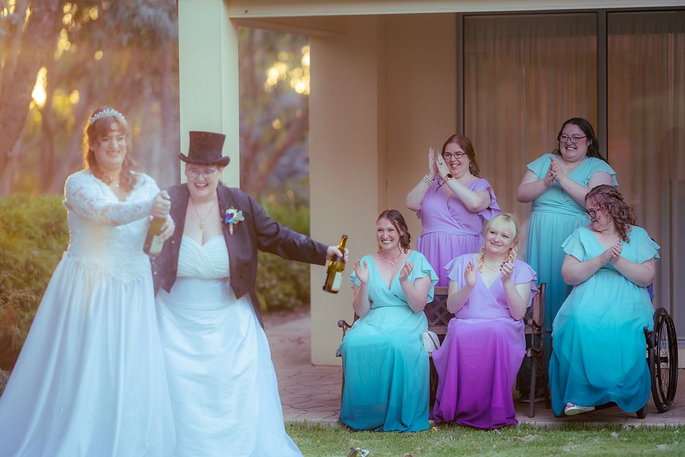 Wedding party in turquoise and purple dresses pose together for outdoor photo session in autumn setting.