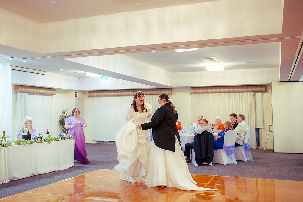 A large empty dance studio with mirrored walls, hardwood floors and wall-mounted barres in neutral colors.