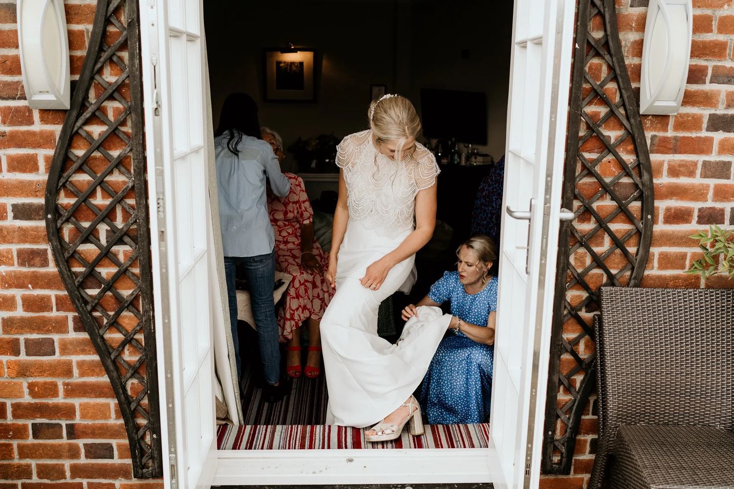 A bride in a white lace dress gets ready in a brick doorway entrance.