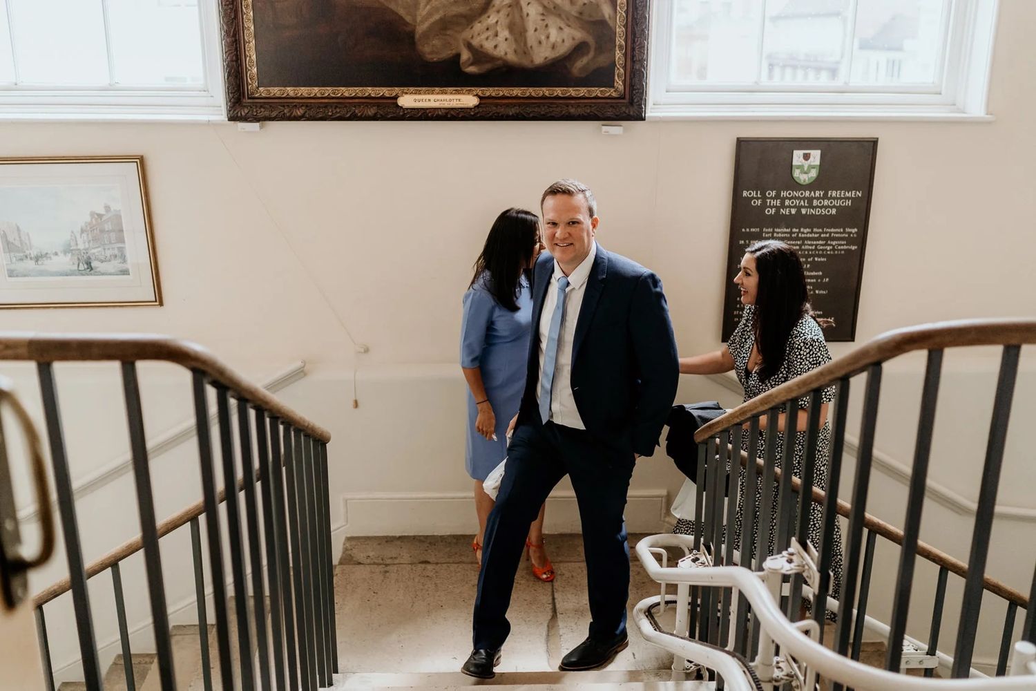 People walking up an elegant staircase inside a historic building.