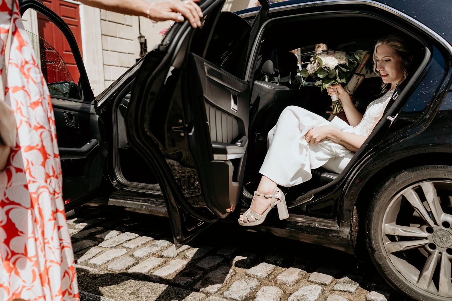 Contemporary black and white wedding party exiting a vehicle onto a cobblestone street.
