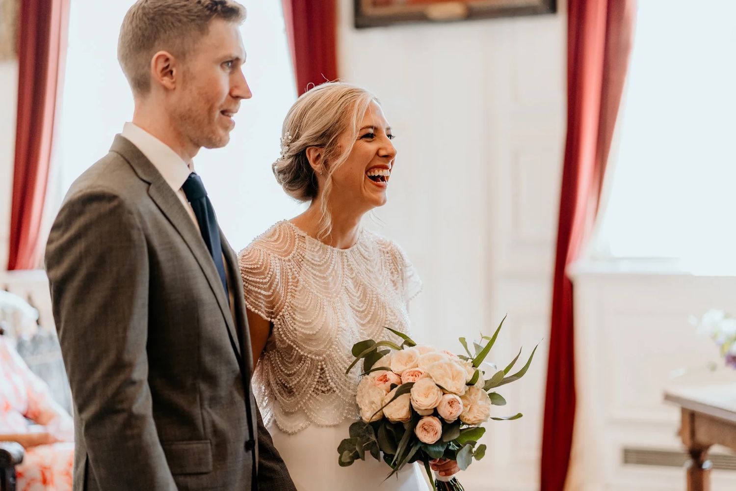 Wedding celebration moment in an ornate room with white walls and red curtains.