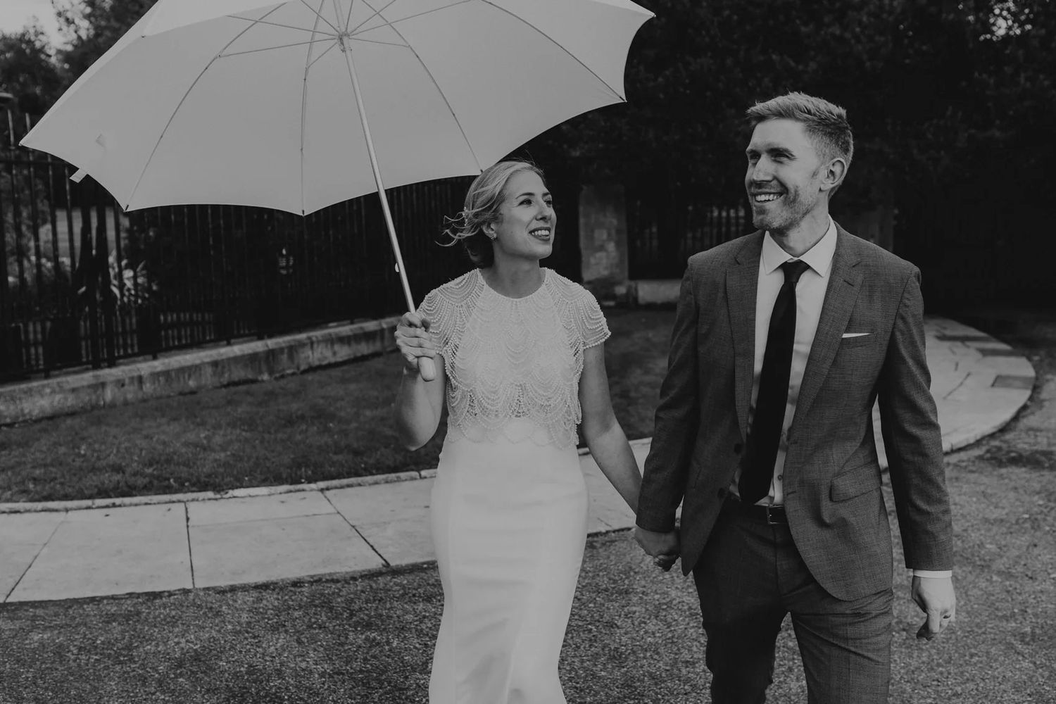 Wedding couple poses with white umbrella during an outdoor photo session in black and white.