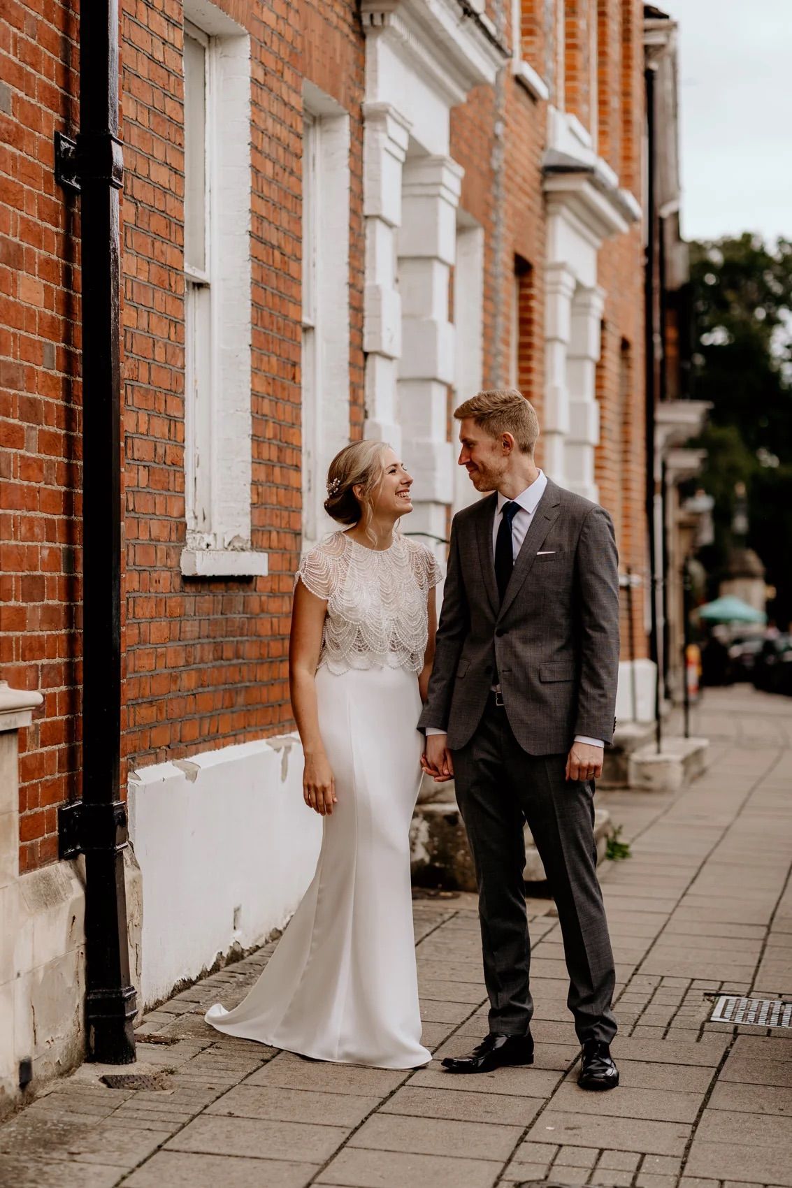A couple shares intimate moments along a red brick wall during a wedding photo session on a city sidewalk.