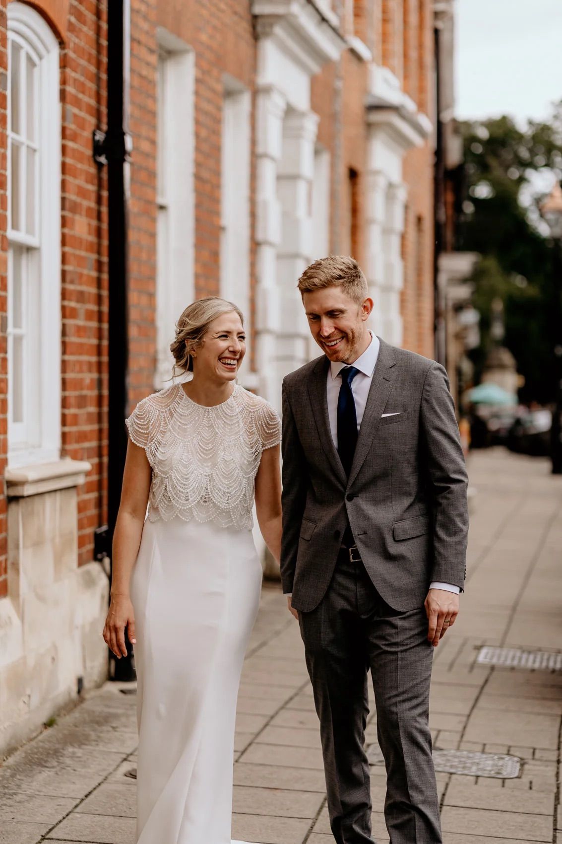A couple shares joyful moments while walking along a historic brick building exterior.