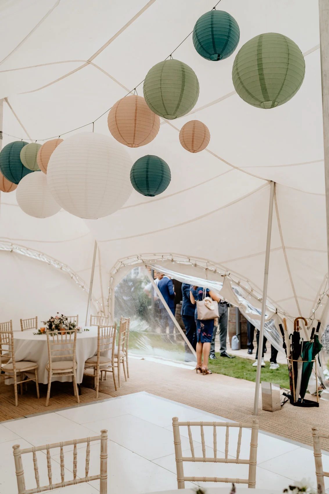 White wedding tent interior decorated with hanging paper lanterns in green, white and peach colors.