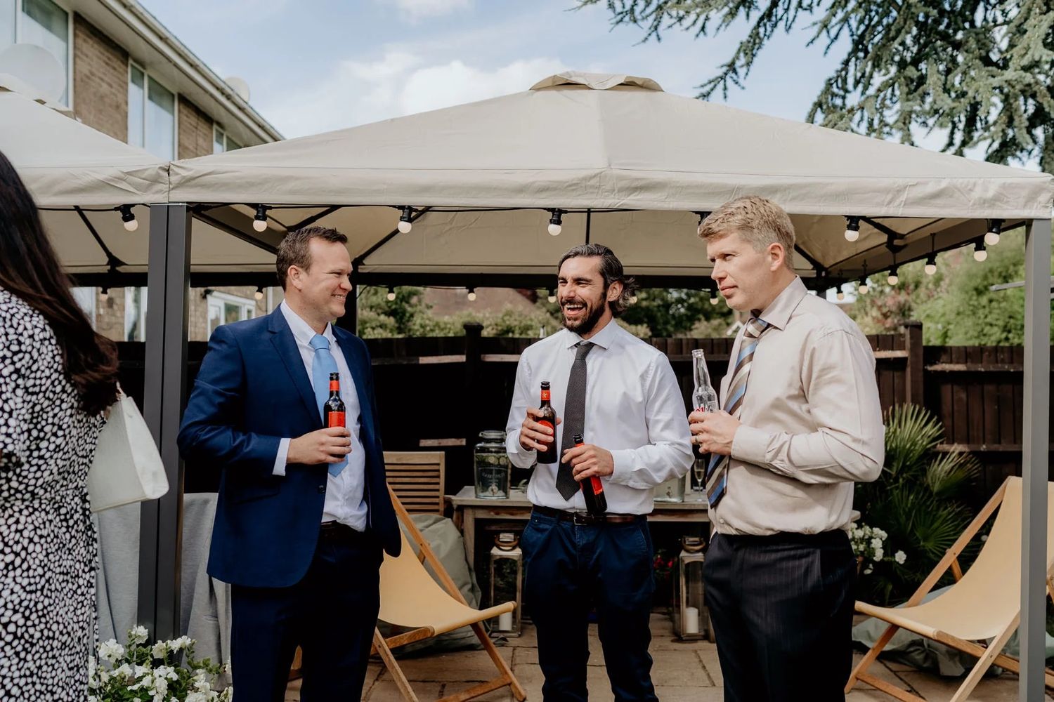 Outdoor wedding reception gathering under tent canopy with guests mingling.