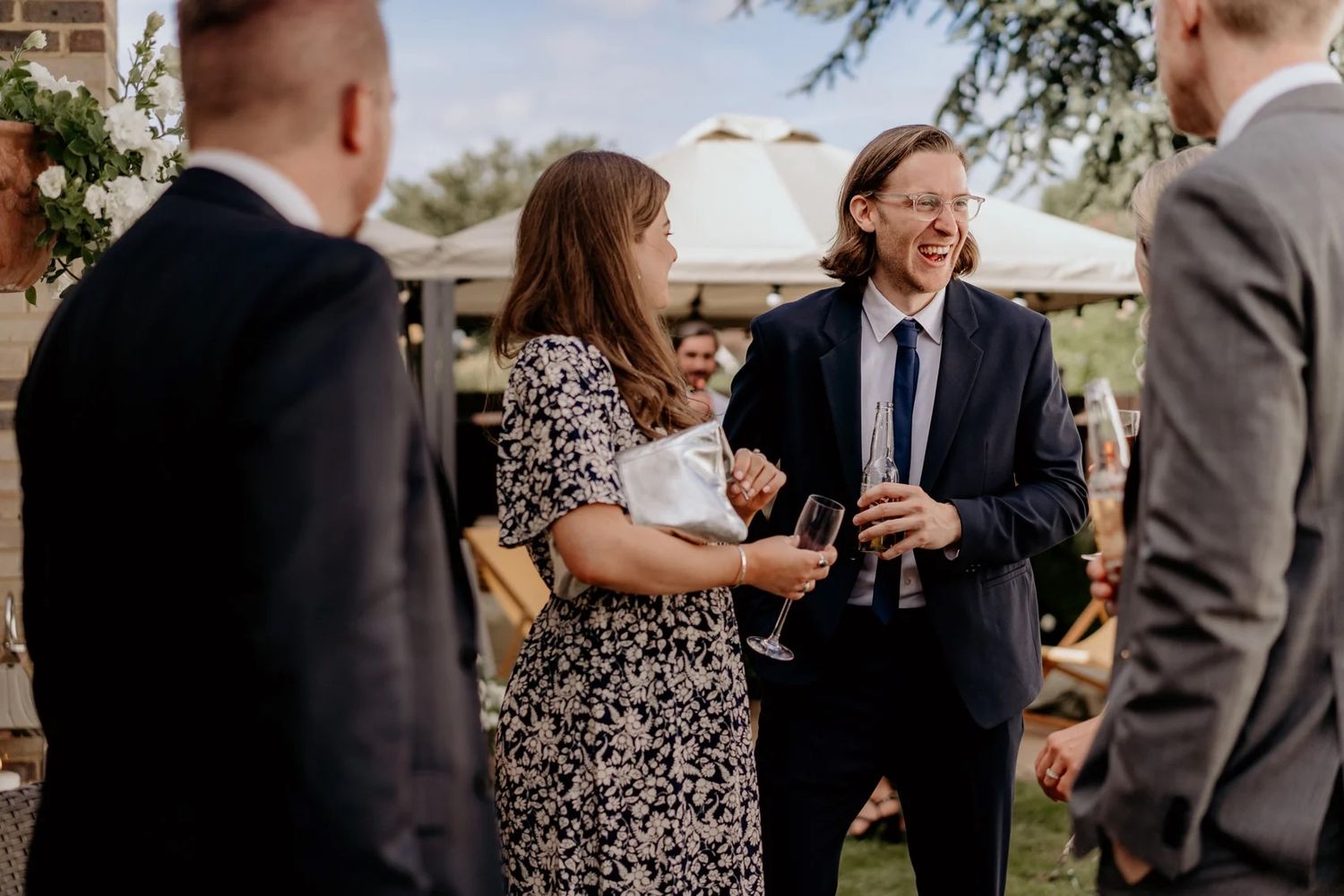 A small group chats and laughs together during an outdoor social gathering with drinks.