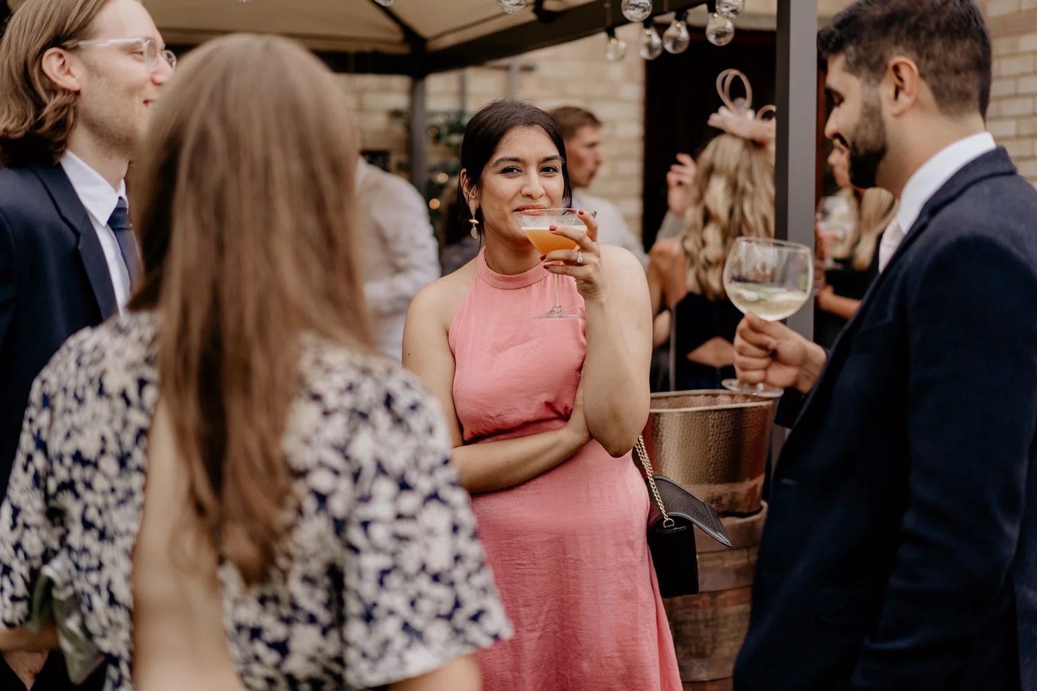 Wedding party members enjoy drinks and conversation at an elegant indoor reception.