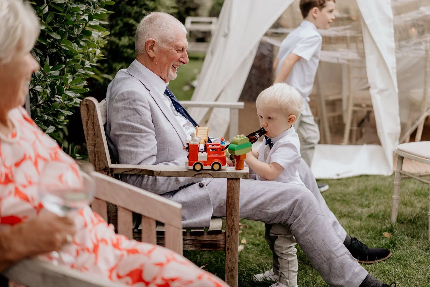 Outdoor wedding reception with guests mingling under white tent covers in a garden setting.