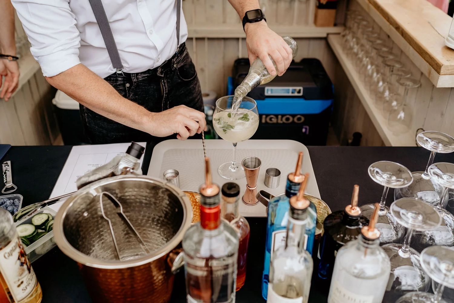 Close-up of bartender preparing cocktails with various bottles and mixers.