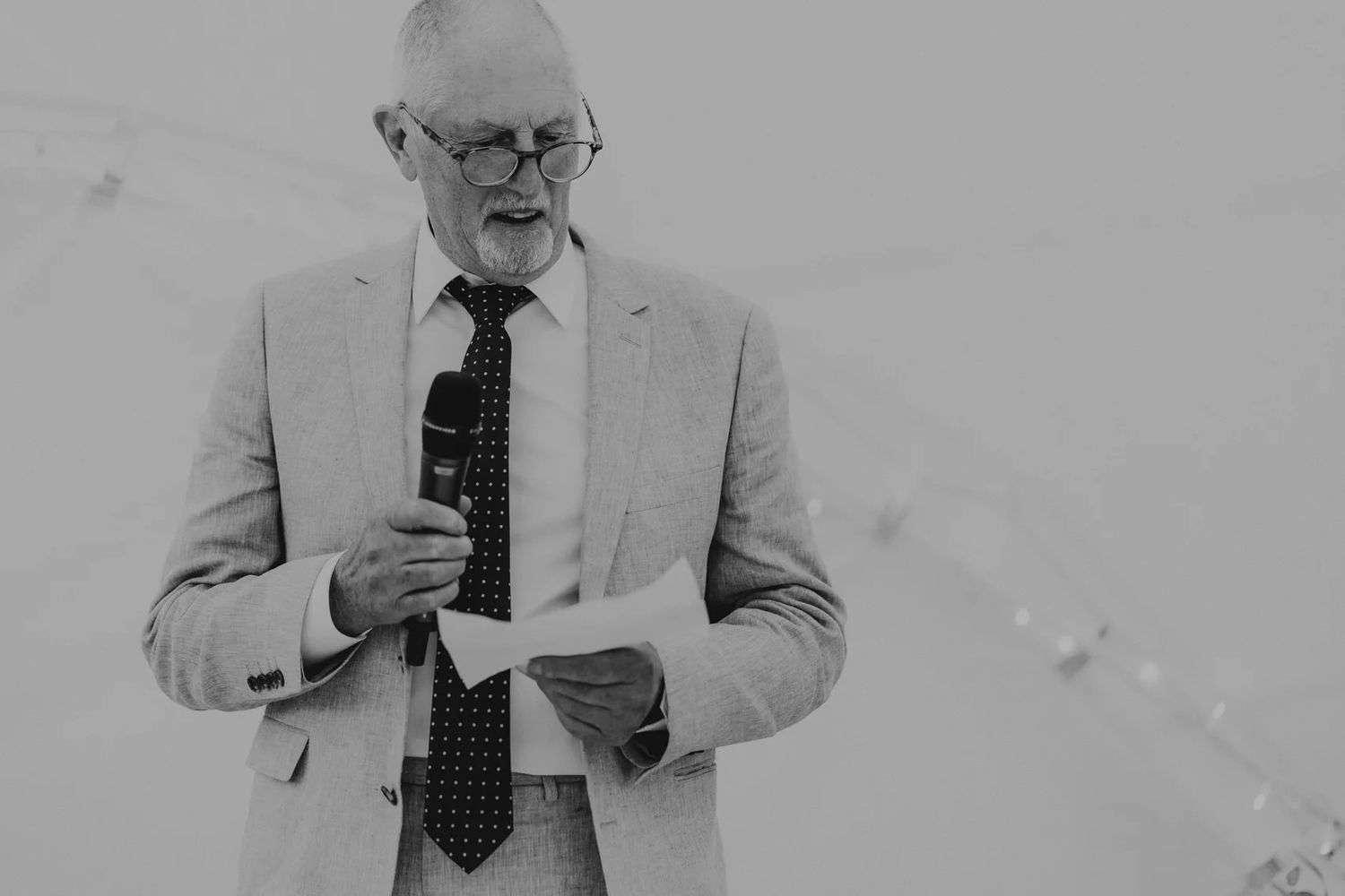 Man in a light suit and tie reading papers while standing against a white background.
