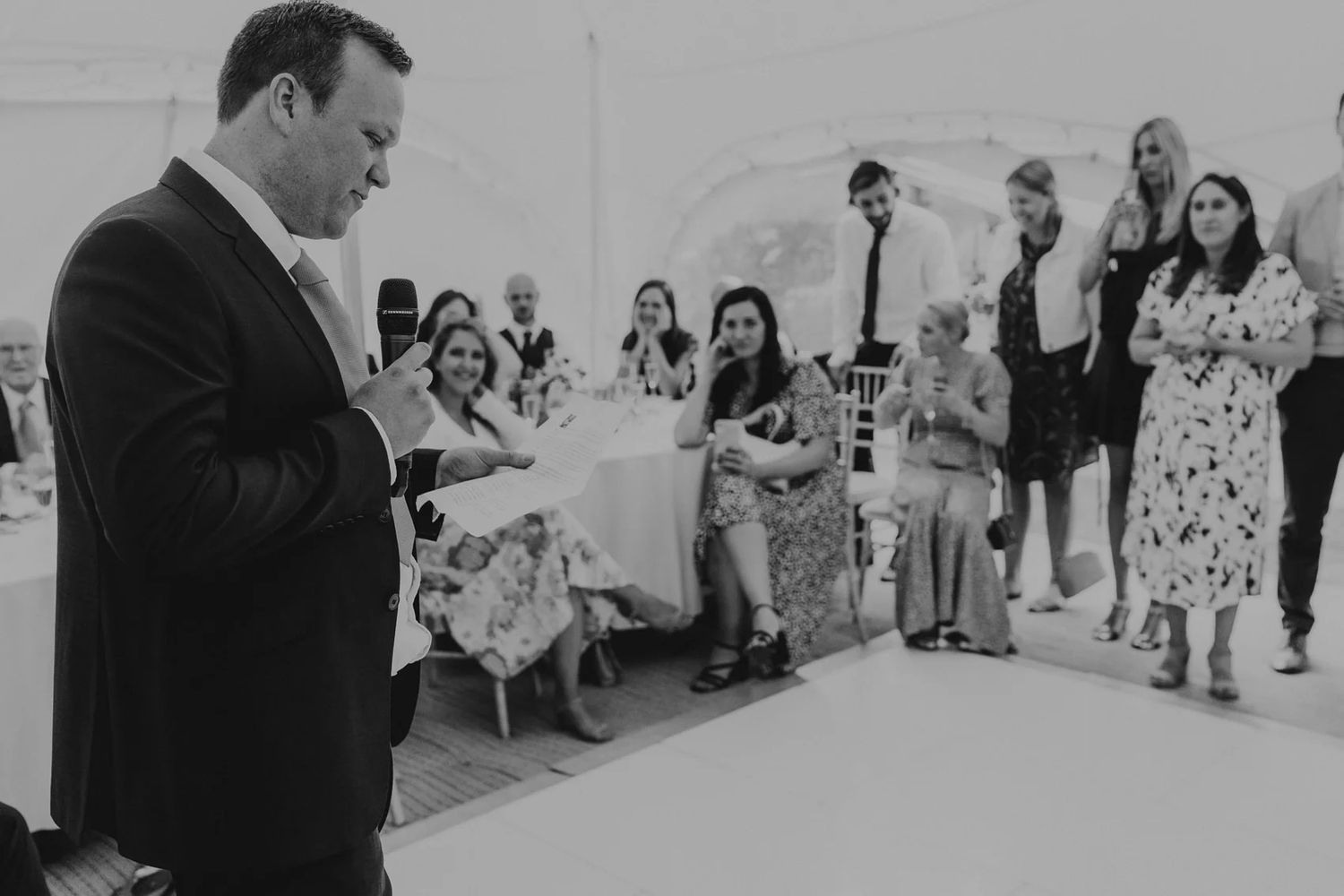 Black and white photo of wedding reception guests under white tent.