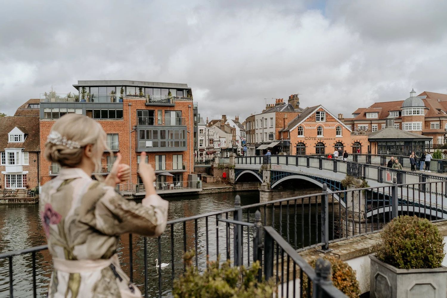 Scenic waterfront view of Windsor town with buildings and bridge visible along the river Thames under cloudy skies.