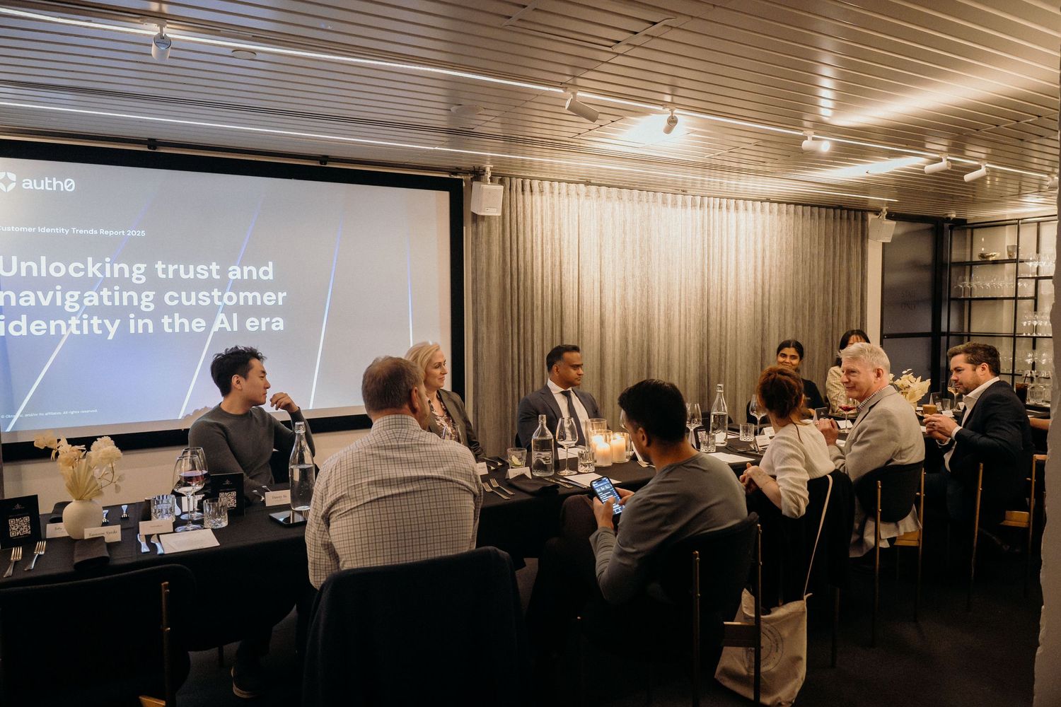 Event participants engage in discussions and presentations in a modern conference room with warm lighting and wooden details.