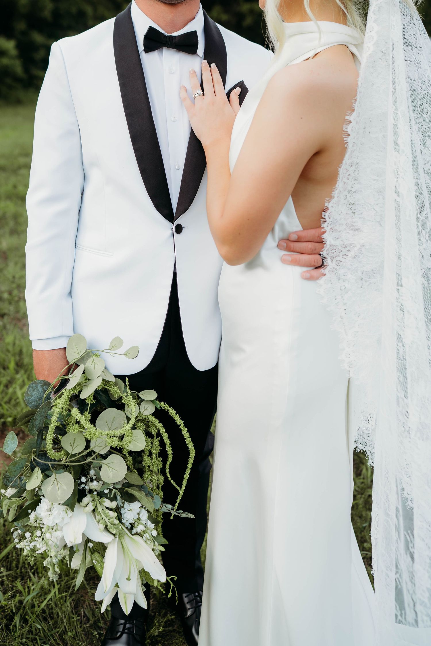 Close-up wedding portrait details showing white tuxedo, bridal dress with veil, and elegant eucalyptus bouquet.