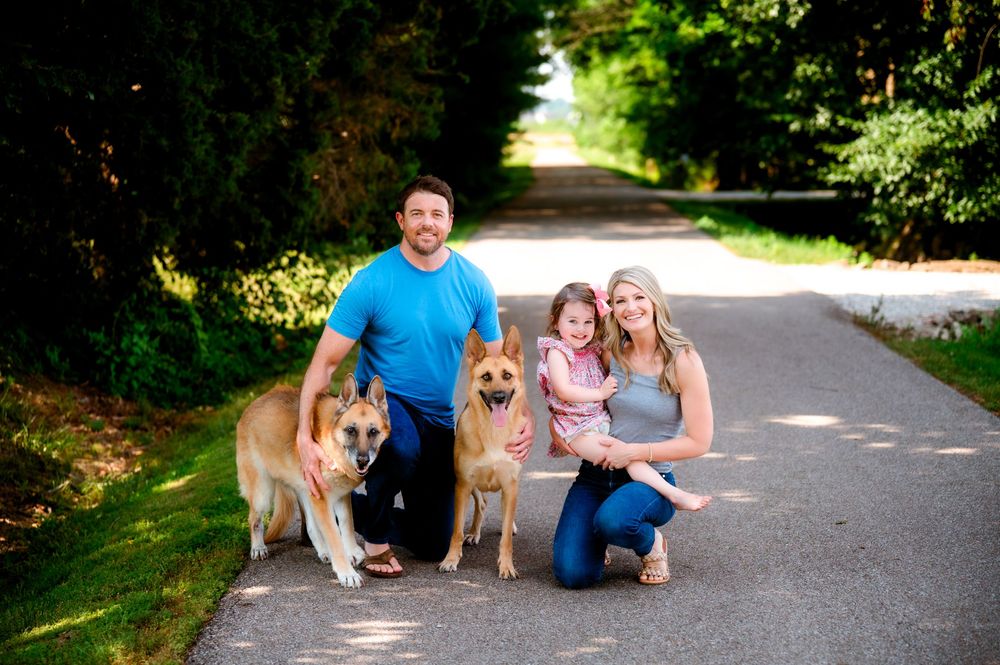 Happy dogs with their owners sitting together on a sunny path in a park setting.
