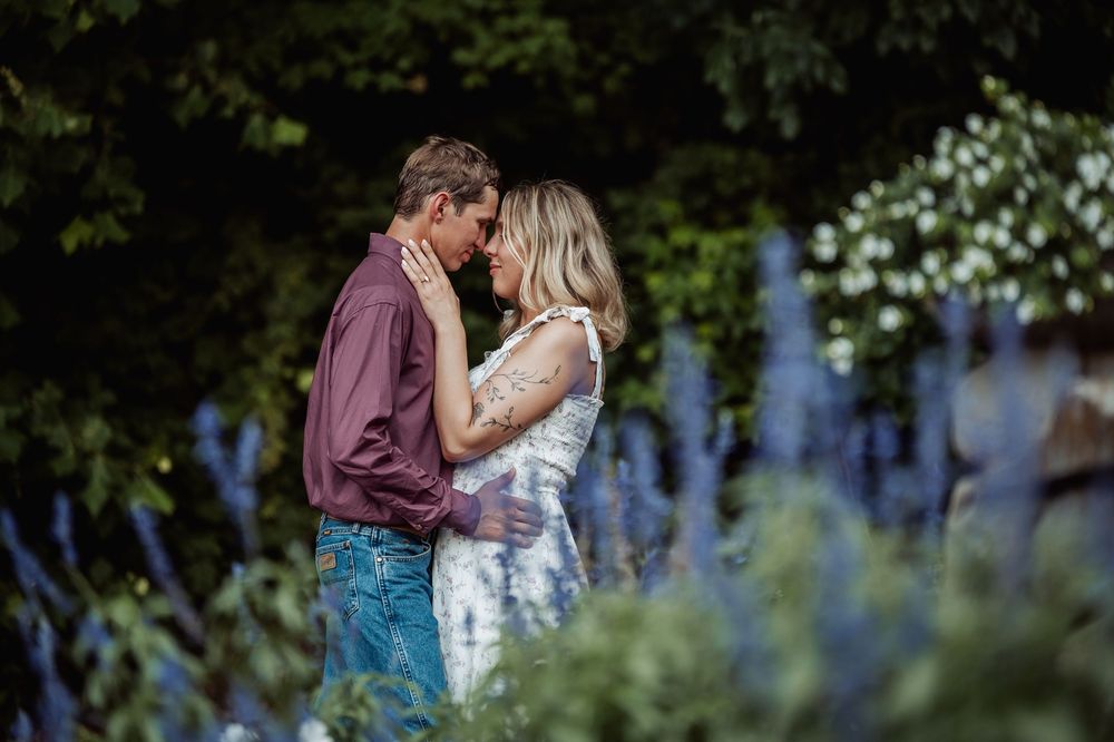 Couple sharing a romantic moment in a lush garden surrounded by blue and white flowers.