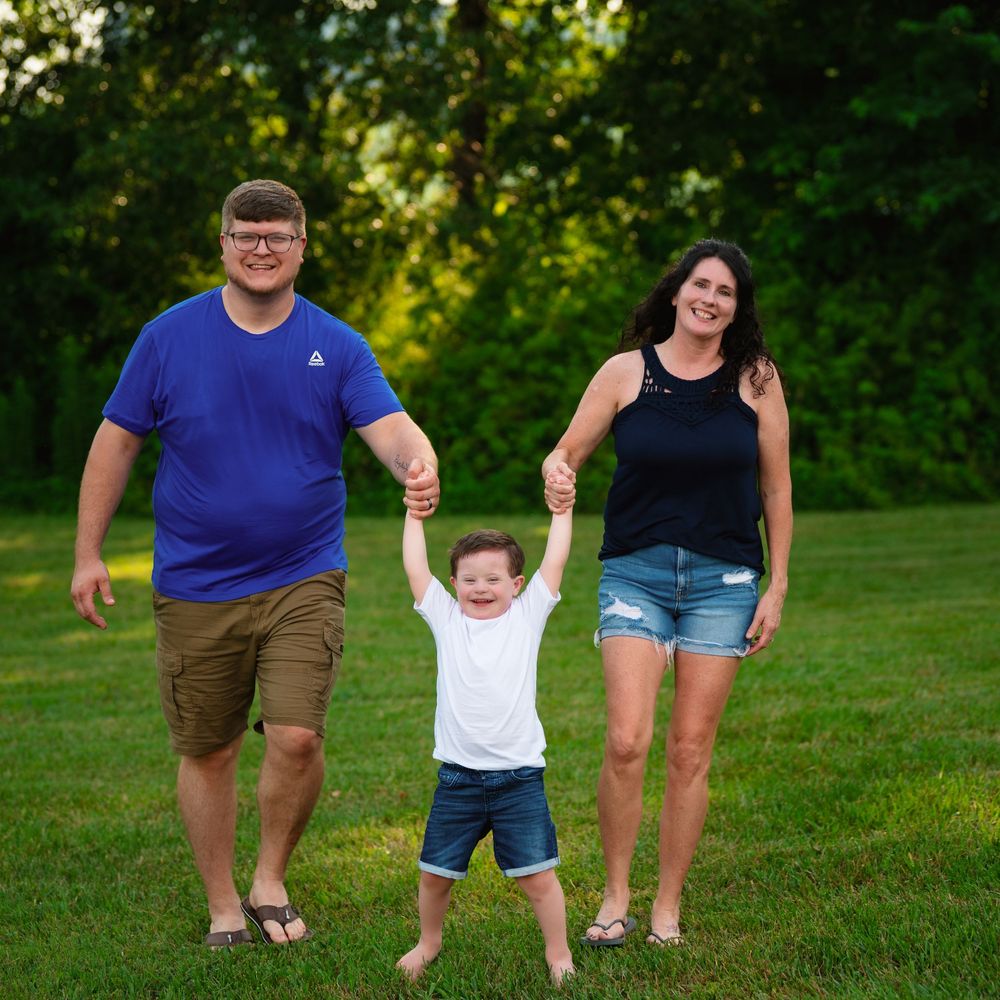 A family holds hands while enjoying a summer evening on a grassy lawn with trees in the background.