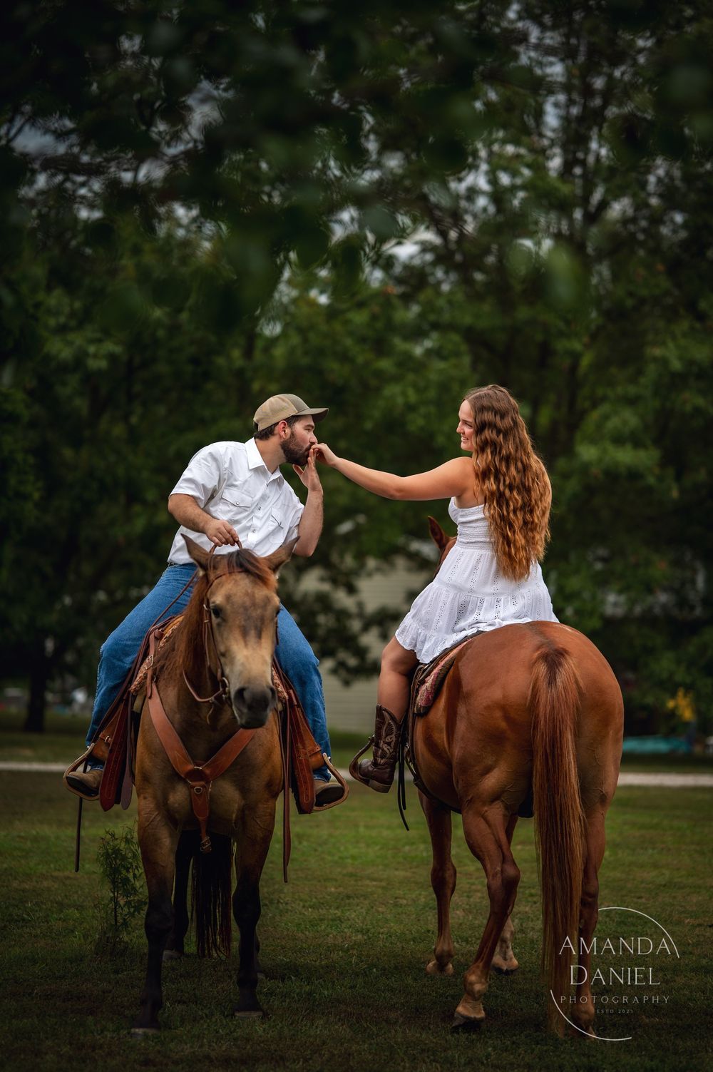 Playful couple on horseback in a green field during a summer photoshoot as the woman playfully pushes the man away.