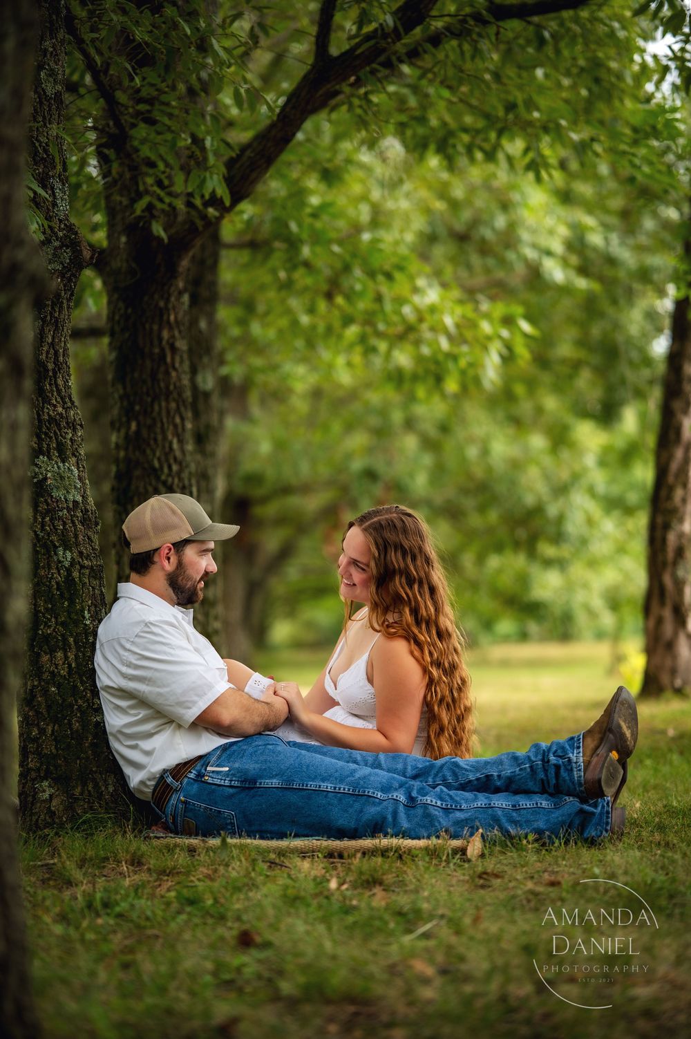 Couple lying together on grass under shady trees in a romantic outdoor photo session.