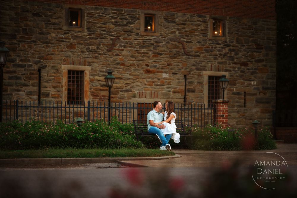 A romantic couple poses along a rustic stone wall with dramatic lighting at sunset for an intimate engagement photo.