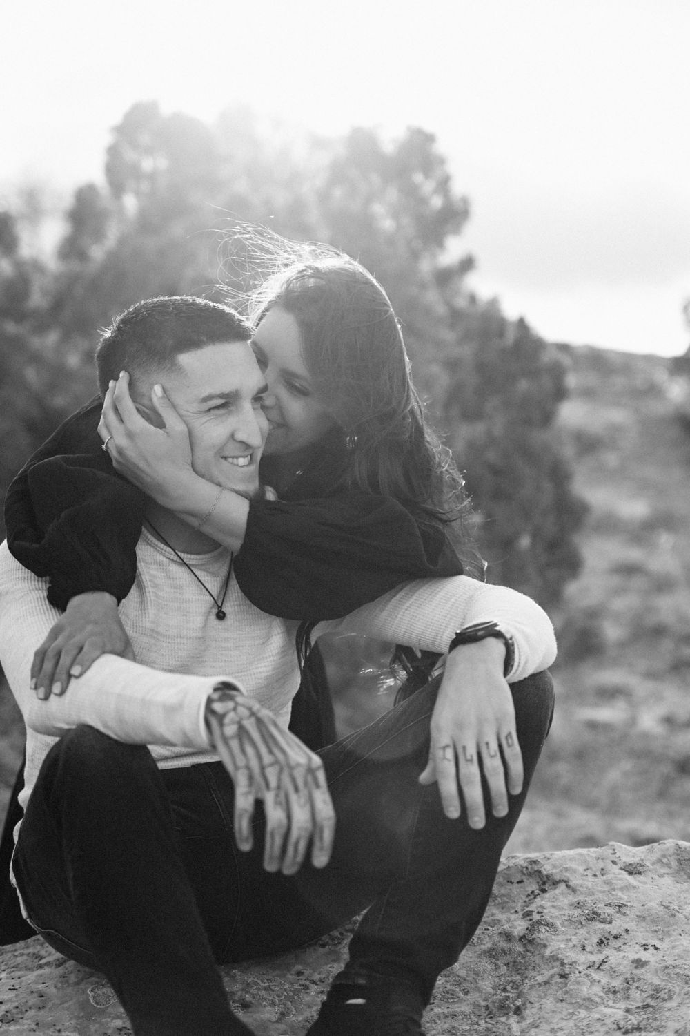 Black and white portrait of couple sharing intimate moment on rocky terrain.