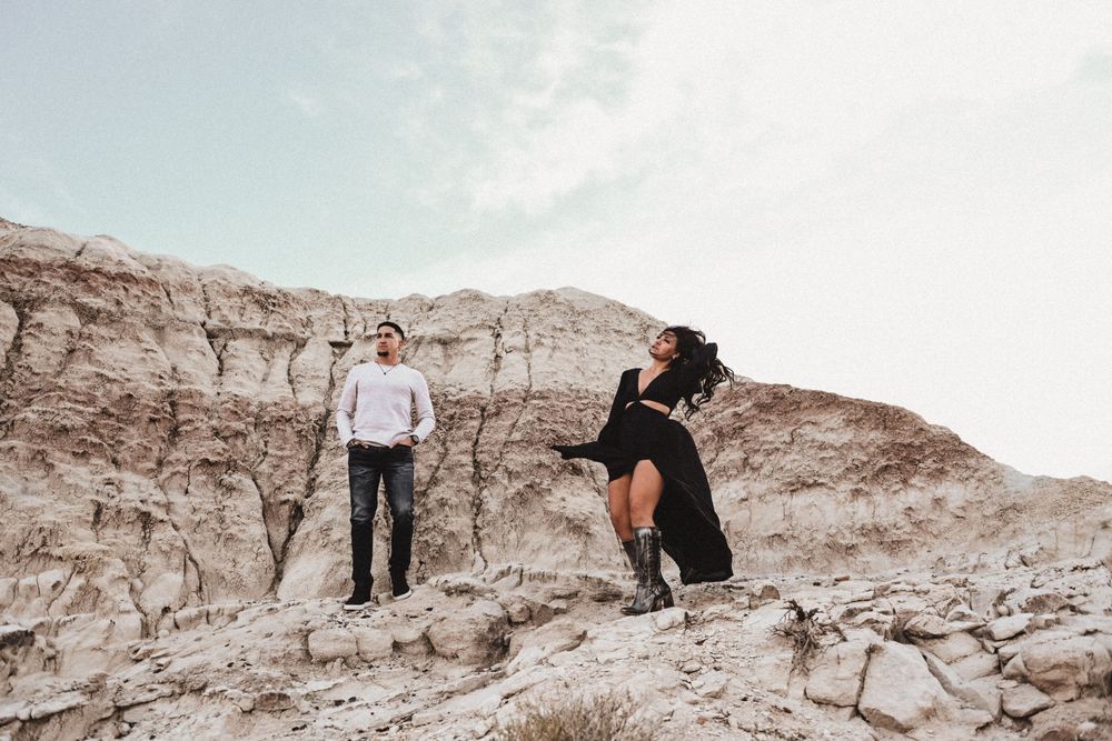 Couple posing on white rocky terrain against bright sky background.