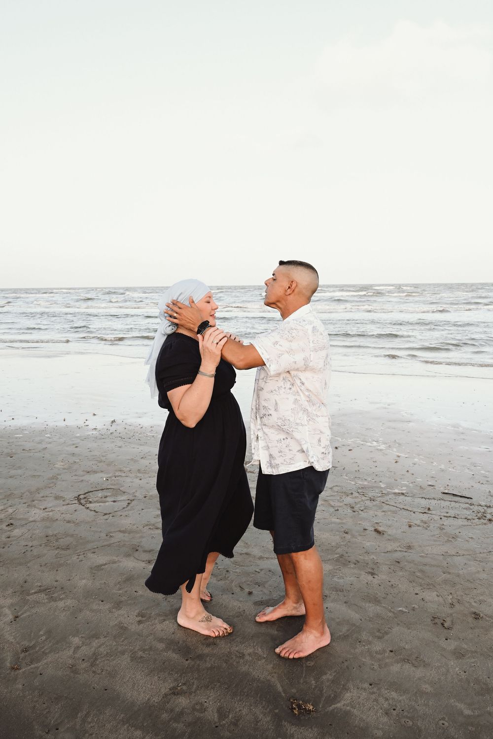 A couple dancing barefoot on a beach at sunset.
