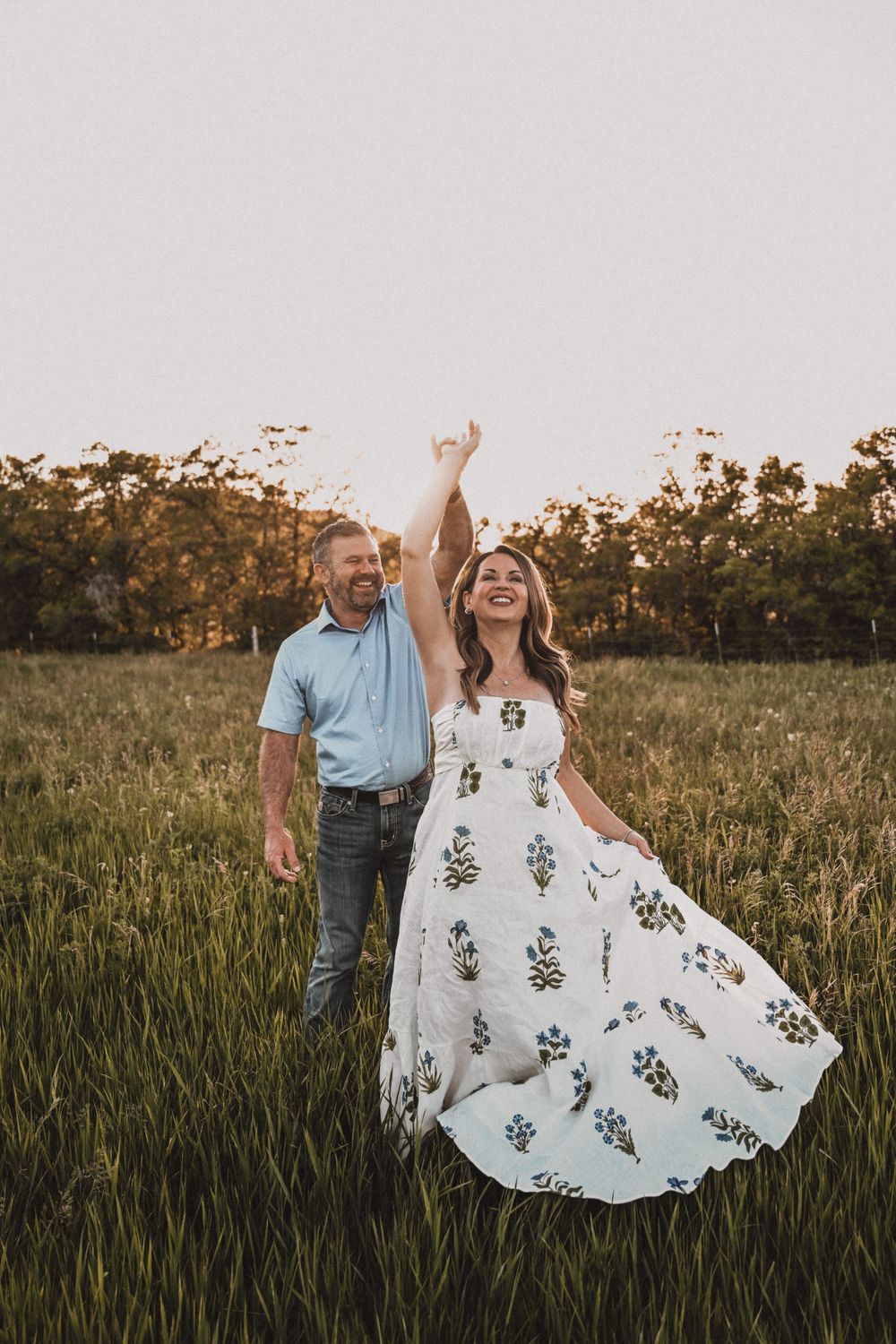 A couple dances in a sunlit field while her floral dress twirls beautifully.
