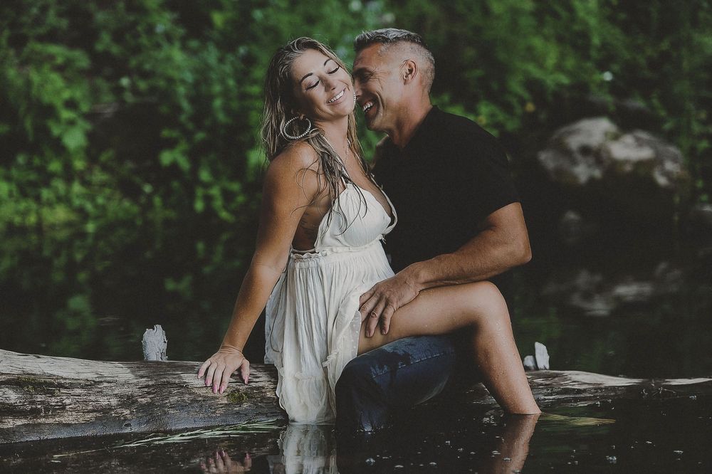 A couple shares romantic moments by a serene lake surrounded by greenery.