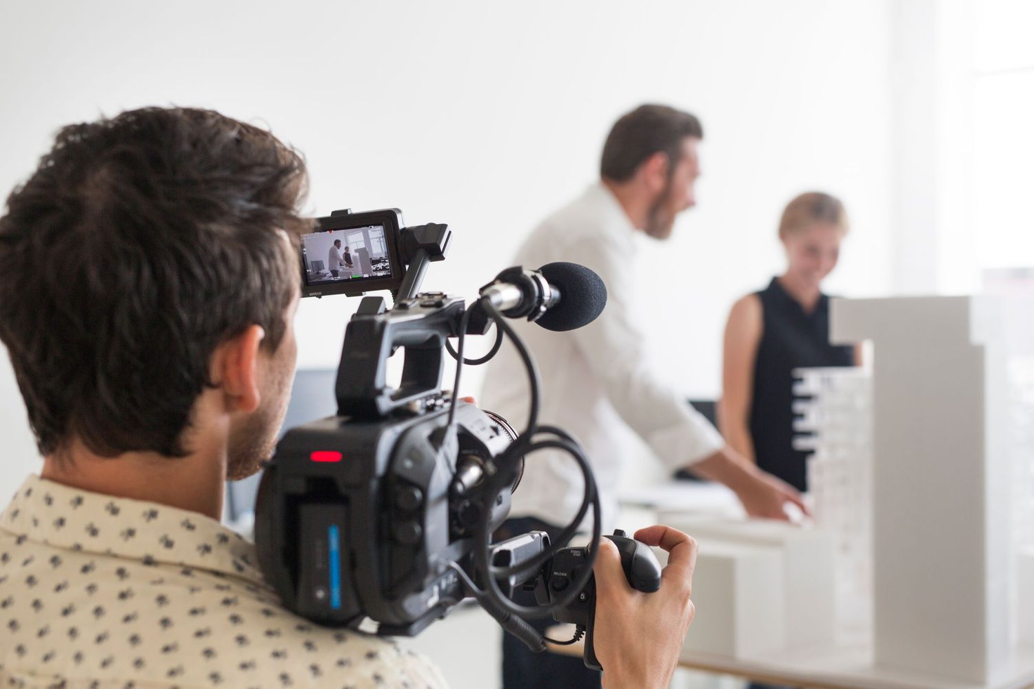 Camera operator filming people during a business video production in a bright office setting.
