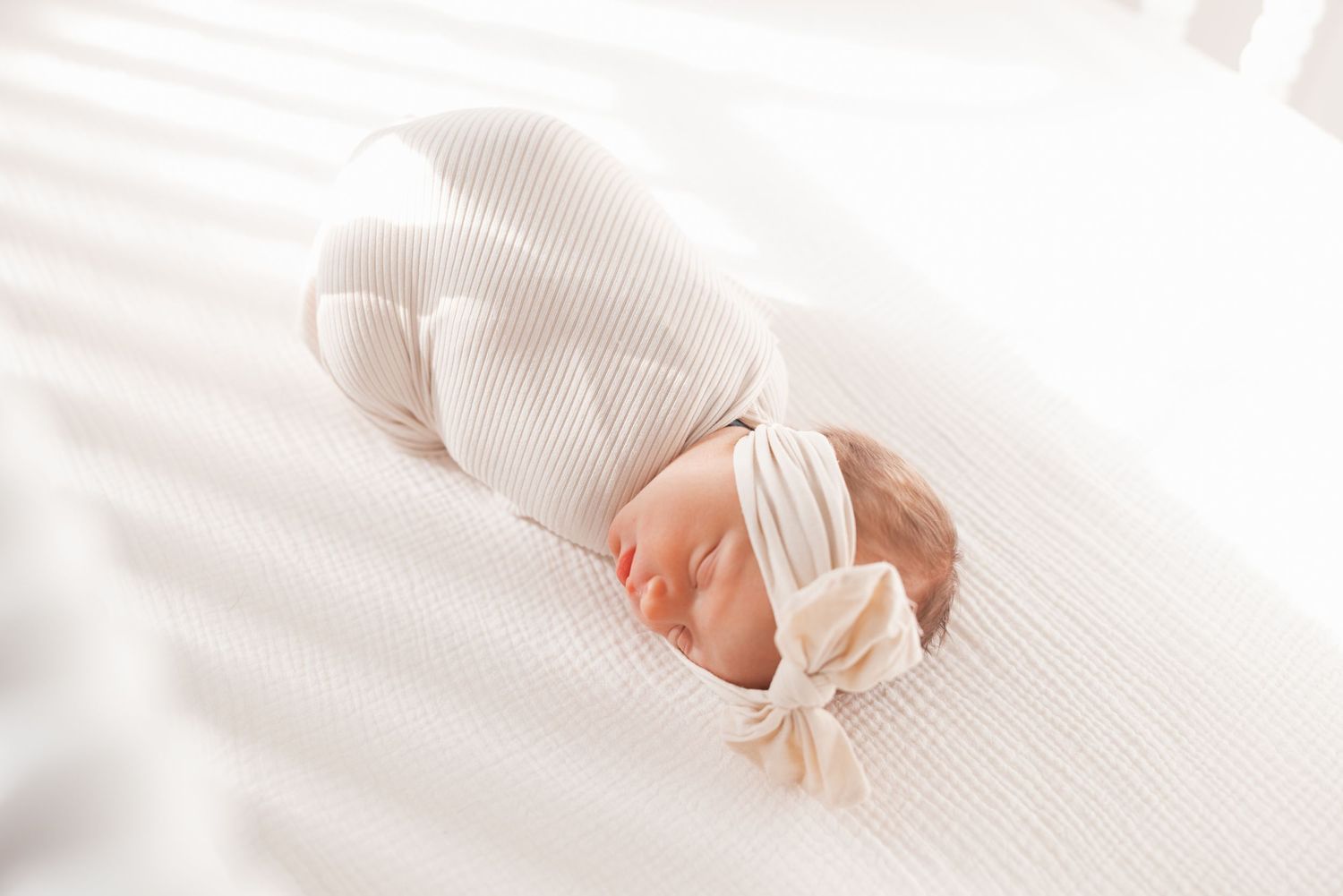 Close-up view of a sleeping newborn baby wrapped in soft white textiles.