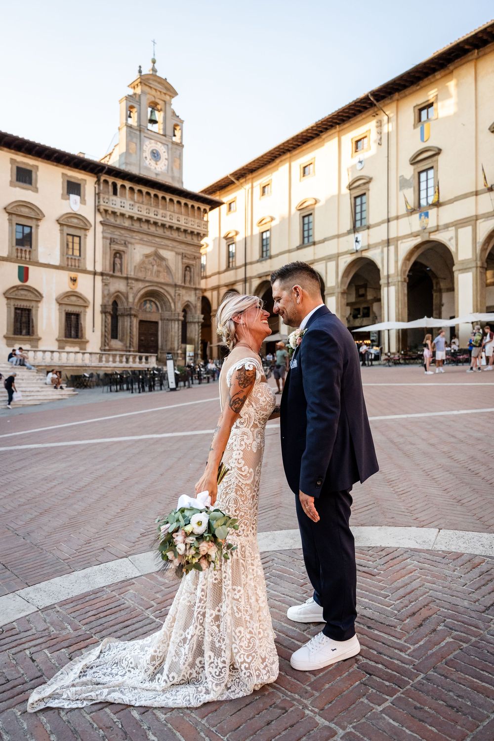 A couple in wedding attire share an intimate moment in a historic Italian plaza with beautiful architecture in Arezzo.