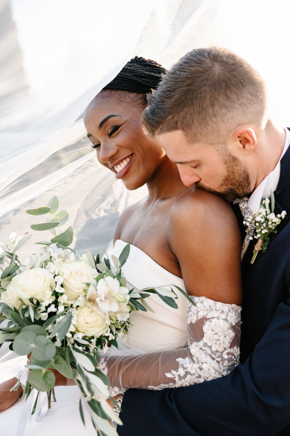Close-up shot of a newlywed couple sharing an intimate moment with white floral bouquet at golden hour.