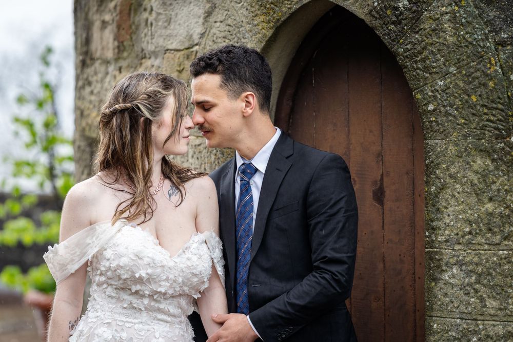 A romantic wedding couple shares an intimate moment in front of a rustic wooden doorway.