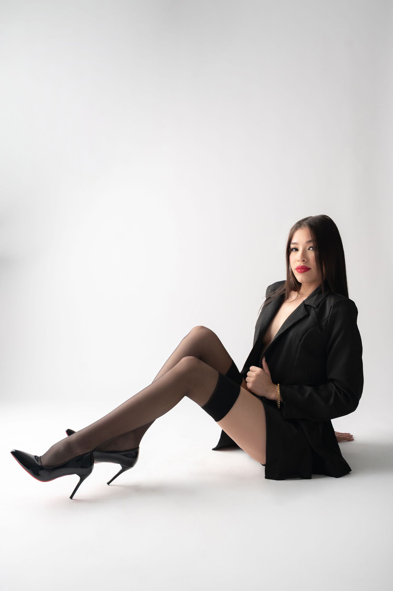 Stylish portrait with black blazer, stockings and high heels against minimalist white backdrop.